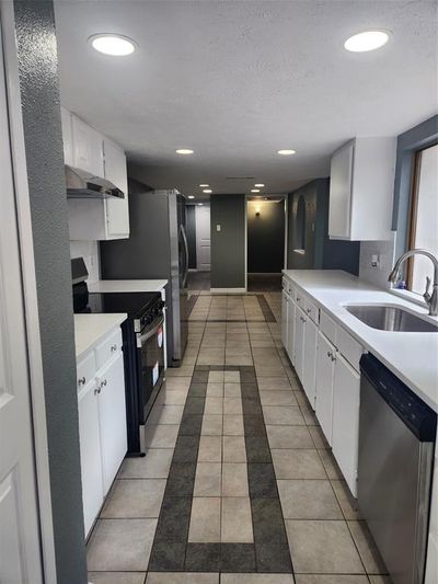 Kitchen with ventilation hood, sink, white cabinets, range, and dishwashing machine | Image 2