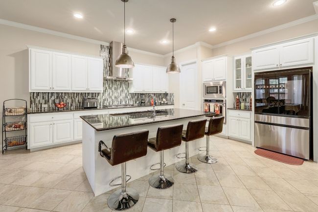 Kitchen with ornamental molding, stainless steel appliances, dark countertops, backsplash, and light tile patterned flooring | Image 14
