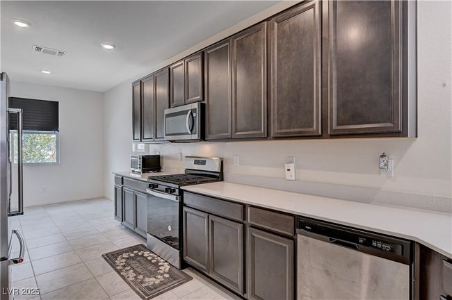 Kitchen featuring appliances with stainless steel finishes, dark brown cabinetry, light countertops, light tile patterned floors, and recessed lighting | Image 16
