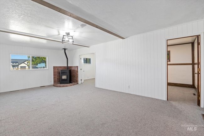 Unfurnished living room featuring a wood stove, a textured ceiling, carpet, and wood walls | Image 8