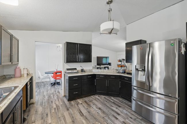Kitchen featuring lofted ceiling, light wood-style flooring, stainless steel fridge, and dark cabinetry | Image 6
