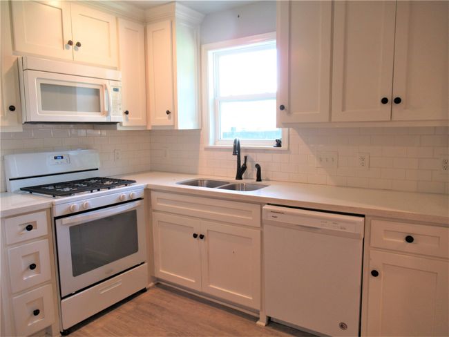 Kitchen with white cabinets, light wood-style flooring, a sink, and white appliances | Image 11
