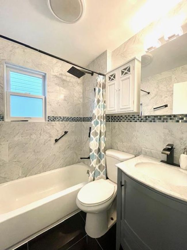 Bathroom with tile walls, shower / bathtub combination with curtain, backsplash, toilet, and vanity | Image 7
