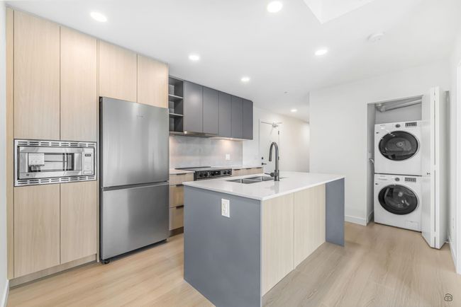 Kitchen with light brown cabinetry, stacked washer and clothes dryer, appliances with stainless steel finishes, modern cabinets, and a sink | Image 4