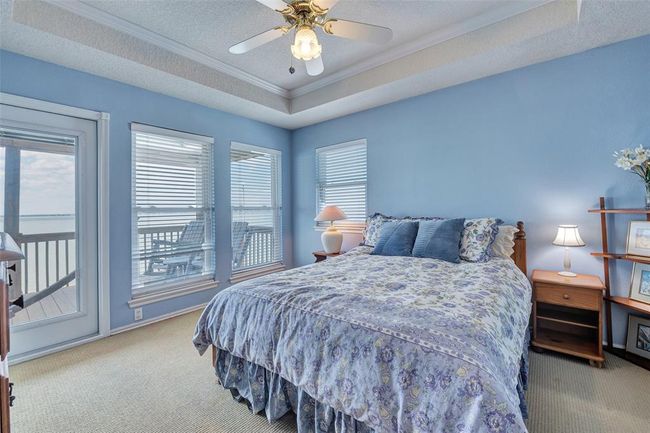 Wake up to stunning water views in this light-filled guest room featuring direct access to the balcony, tray ceiling detail, and peaceful coastal tones. A perfect retreat for visitors or family. | Image 20
