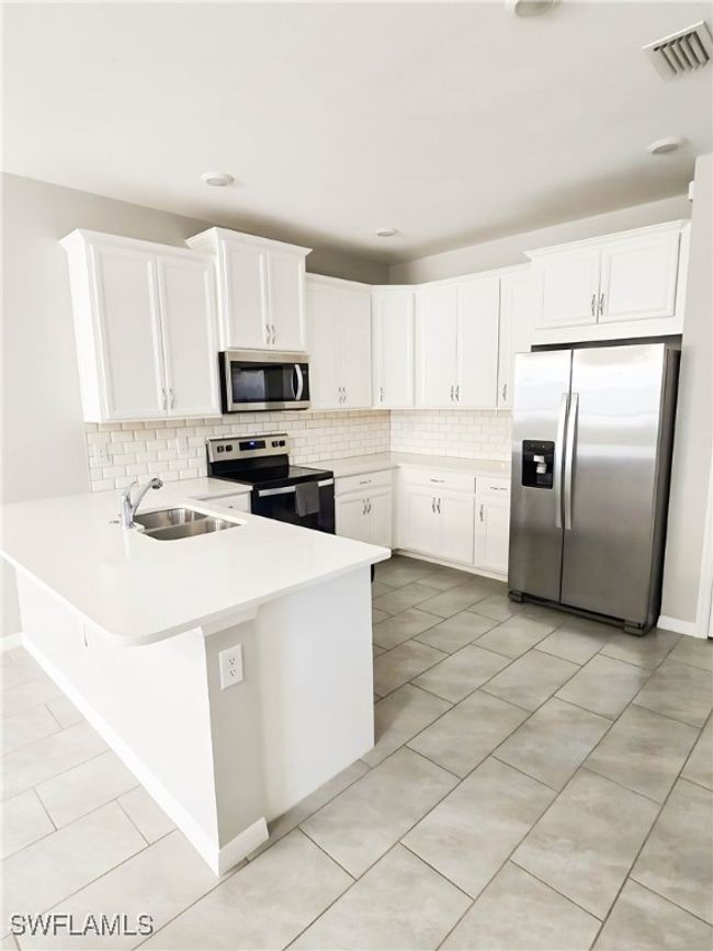 Kitchen featuring appliances with stainless steel finishes, a sink, tasteful backsplash, a peninsula, and light countertops | Image 12