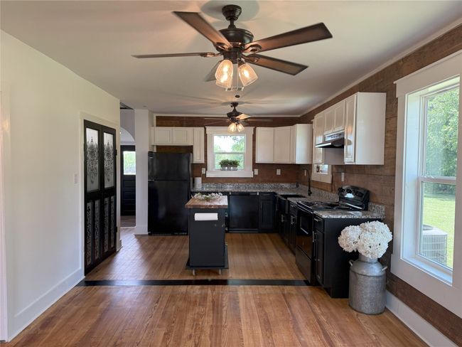 Kitchen featuring black appliances, under cabinet range hood, a kitchen island, white cabinets, and a ceiling fan | Image 5