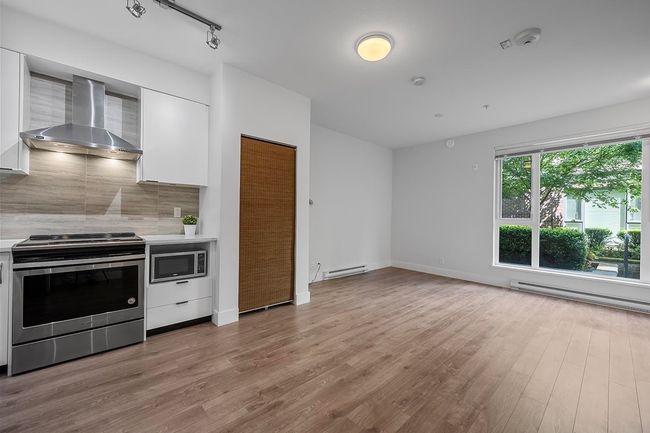 Kitchen featuring appliances with stainless steel finishes, wall chimney range hood, baseboard heating, and white cabinetry | Image 12