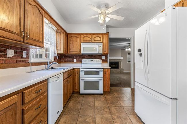 Kitchen featuring white appliances, ceiling fan, brown cabinets, and a sink | Image 34