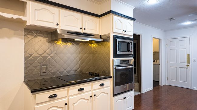 Kitchen with dark wood-style floors, dark countertops, under cabinet range hood, decorative backsplash, and stainless steel appliances | Image 17