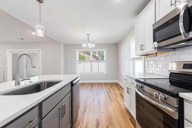 Kitchen featuring stainless steel appliances, gray cabinets, pendant lighting, light countertops, and tasteful backsplash | Image 13