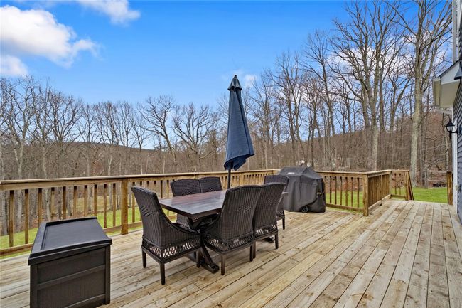 Wooden terrace featuring outdoor dining space, grilling area, and a view of trees | Image 34