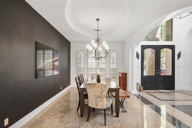 Ideal for casual to formal entertaining, the dining room with tray ceiling & chandelier lighting includes pre-wiring for ceiling speakers, arched windows with plantation shutters overlooking the front yard, painted accent wall & tile flooring. | Image 5