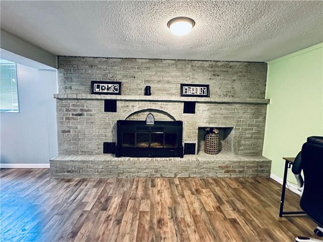 Detailed view of a brick fireplace, wood finished floors, a textured ceiling, and baseboards | Image 20