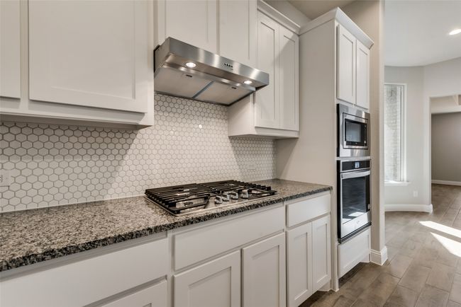 Kitchen featuring gas stove, stainless steel appliances, white cabinetry, ventilation hood, and light stone counters | Image 8