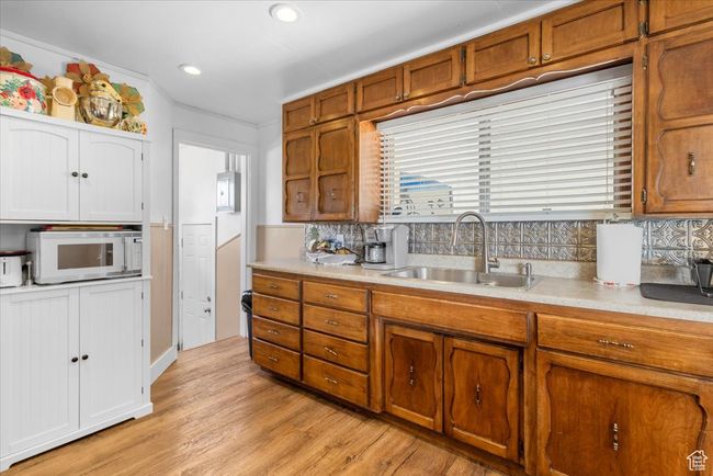 Kitchen with light countertops, light wood-type flooring, a sink, white microwave, and brown cabinetry | Image 27