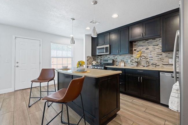 Kitchen with stainless steel appliances, backsplash, light countertops, wood tiled floors, and a center island | Image 27