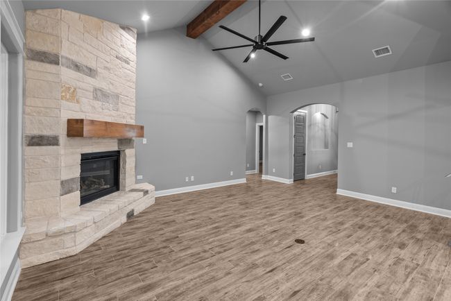 Unfurnished living room with ceiling fan, arched walkways, beamed ceiling, wood finished floors, and a stone fireplace | Image 9
