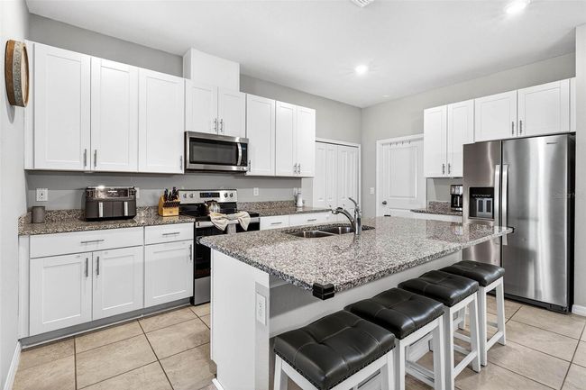 Your kitchen has white shaker cabinetry, quartz countertops, stainless steel appliances, and island seating. Closet pantry and laundry room. | Image 8