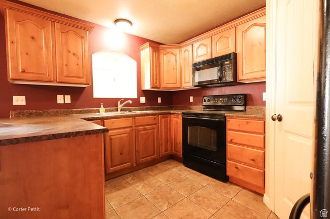 Kitchen with black appliances, light tile patterned floors, and dark countertops | Image 21