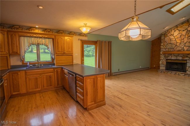 Kitchen with a sink, stainless steel dishwasher, baseboard heating, brown cabinetry, and vaulted ceiling | Image 4