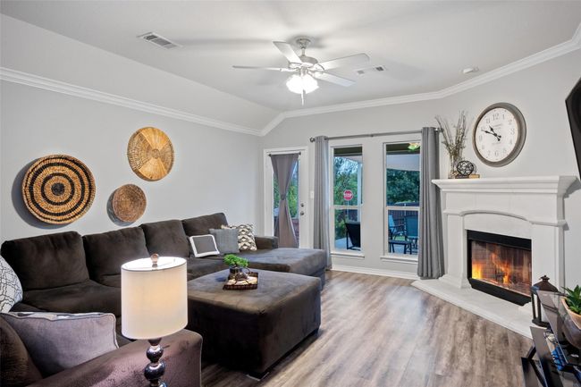 Living room featuring wood finished floors, ceiling fan, ornamental molding, a lit fireplace, and vaulted ceiling | Image 9