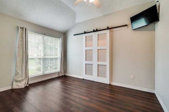 Empty room featuring a textured ceiling, a barn door, vaulted ceiling, dark wood-style flooring, and a ceiling fan | Image 14