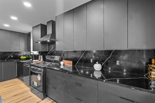 Kitchen with black gas range, wall chimney exhaust hood, a sink, gray cabinetry, and recessed lighting | Image 15