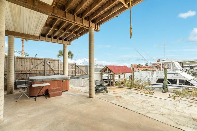 This photo showcases a waterfront patio area with a covered space featuring a hot tub, outdoor seating, and a view of the marina. It offers a relaxing and inviting setting, perfect for enjoying coastal living. | Image 35