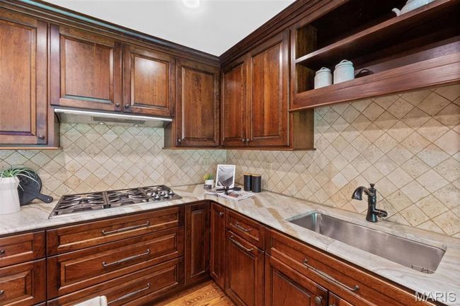 Kitchen featuring stainless steel gas cooktop, backsplash, and light stone counters | Image 22