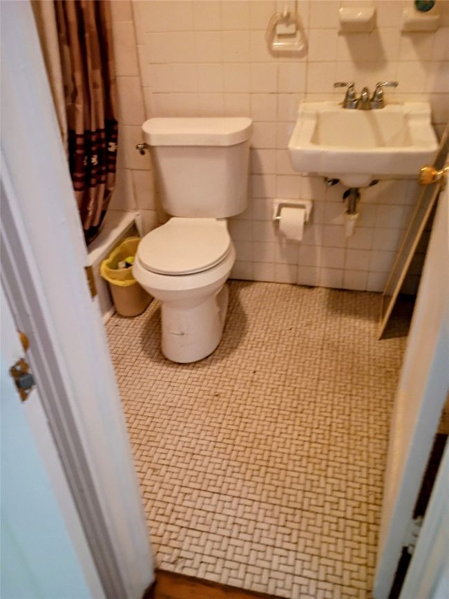 Bathroom with toilet, a sink, curtained shower, and tile walls | Image 6