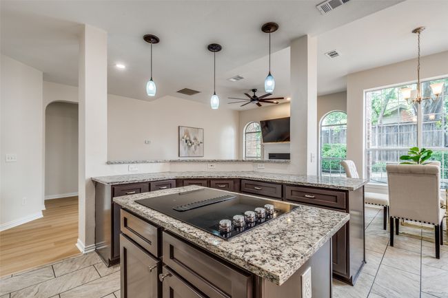Kitchen with black electric cooktop, arched walkways, a kitchen island, a chandelier, and a ceiling fan | Image 11