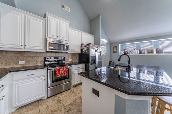 Kitchen with stainless steel appliances, a sink, vaulted ceiling, decorative backsplash, and white cabinetry | Image 7