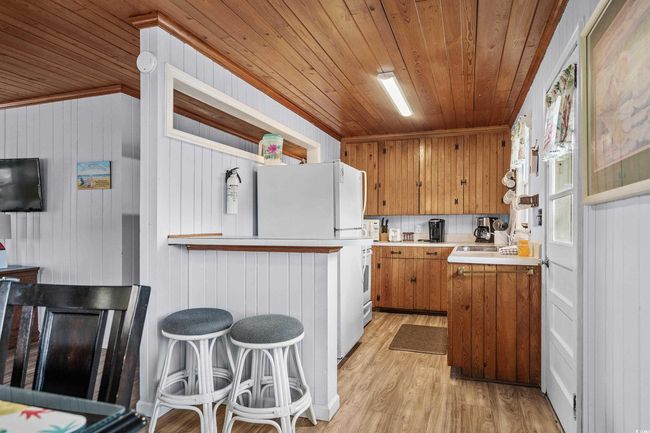 Kitchen featuring brown cabinetry, wooden ceiling, light countertops, light wood-style flooring, and wood walls | Image 18
