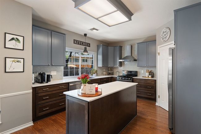 Kitchen featuring light countertops, dark wood-style floors, visible vents, wall chimney range hood, and appliances with stainless steel finishes | Image 10