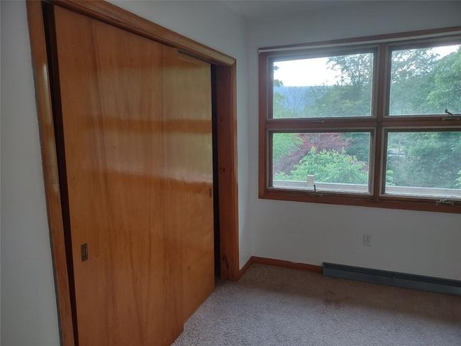 Unfurnished bedroom featuring carpet flooring, a baseboard radiator, a closet, and multiple windows | Image 13