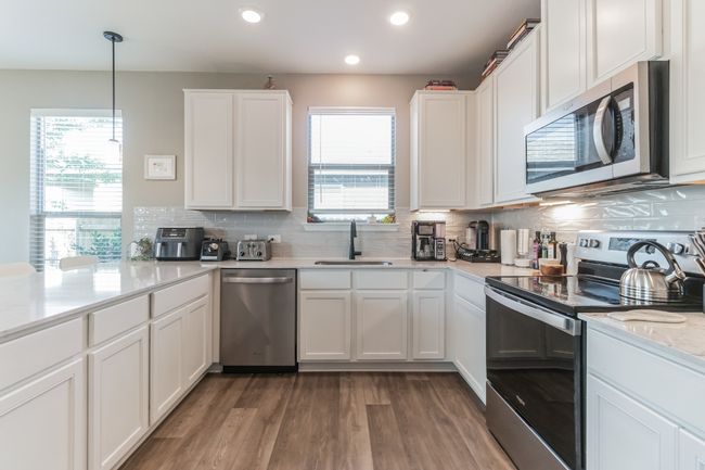 Kitchen featuring appliances with stainless steel finishes, wood finished floors, decorative backsplash, recessed lighting, and white cabinetry | Image 12