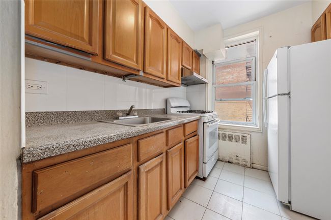 Kitchen featuring white appliances, under cabinet range hood, light tile patterned flooring, and brown cabinetry | Image 11