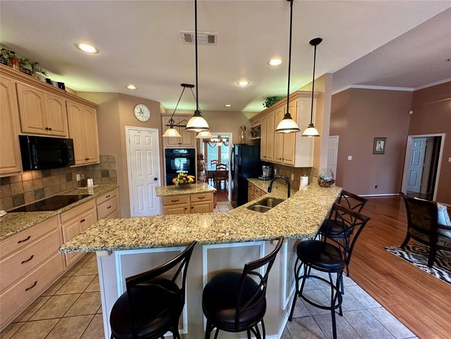 Kitchen featuring visible vents, light brown cabinets, a sink, black appliances, and a kitchen breakfast bar | Image 8