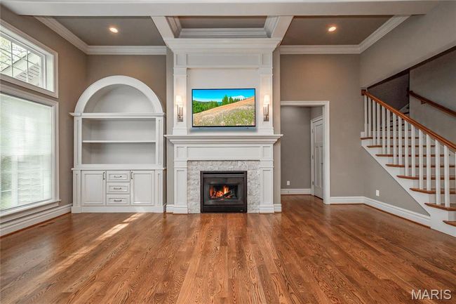 Living room with wood finished floors, stairs, ornamental molding, a stone fireplace, and baseboards | Image 20
