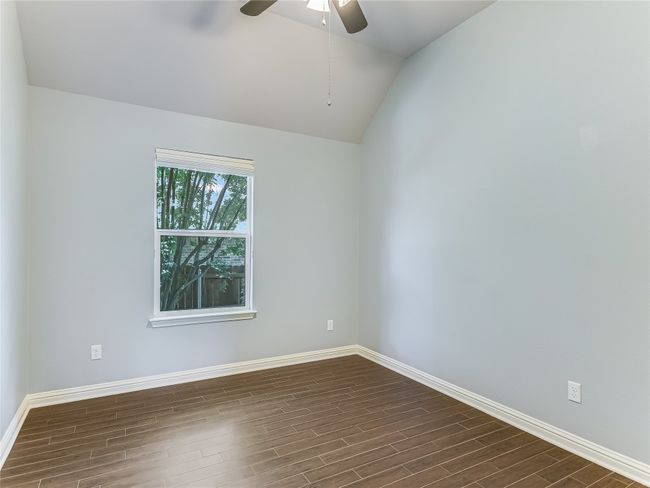 Secondary bedroom with porcelain plank floors, ceiling fan, window shade and closet. | Image 19