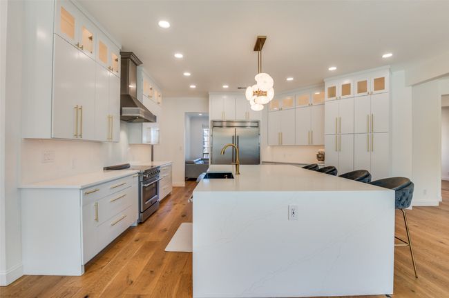 Kitchen with high end appliances, a sink, a large island, light wood-type flooring, and wall chimney range hood | Image 6