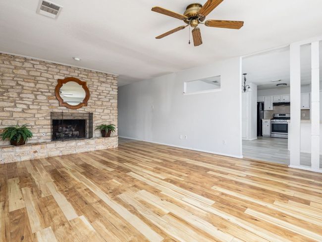 Unfurnished living room featuring light wood-style flooring, a ceiling fan, and a stone fireplace | Image 6
