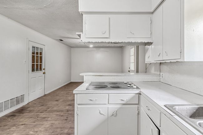 Kitchen featuring black electric cooktop, light wood-style floors, white cabinets, light countertops, and a peninsula | Image 18