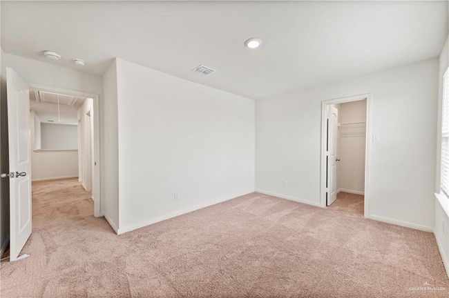 Unfurnished bedroom featuring attic access, light colored carpet, a walk in closet, and baseboards | Image 27