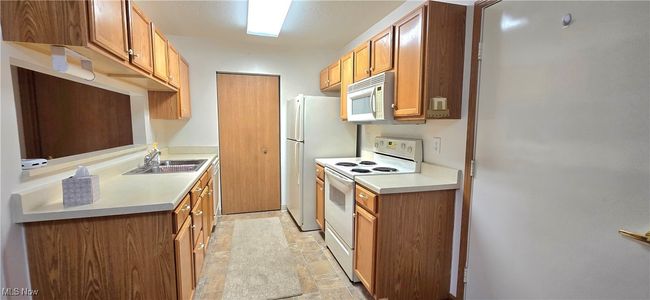 Kitchen featuring white appliances, a sink, light stone finish flooring, light countertops, and brown cabinets | Image 7