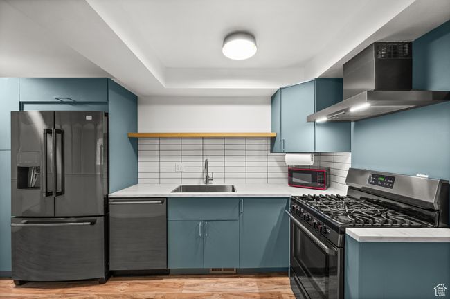 Kitchen featuring appliances with stainless steel finishes, a sink, wall chimney range hood, tasteful backsplash, and blue cabinets | Image 8
