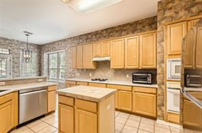 Kitchen featuring white appliances, light tile patterned floors, light brown cabinets, light countertops, and wallpapered walls | Image 7
