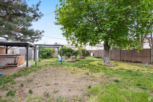 View of yard featuring a gazebo, fence private yard, a fire pit, a hot tub, and a storage unit | Image 20