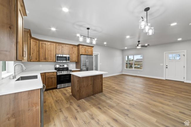 Kitchen featuring decorative light fixtures, stainless steel appliances, a center island, a sink, and brown cabinets | Image 14